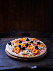 Pizza with salami, mozzarella cheese, black olives and pepper. Rustic wooden background. Soft focus. Copy space.	