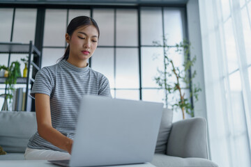 Asian woman sitting on sofa with shopping bags on table her using laptop shopping online in living room at home