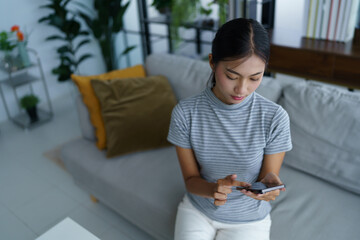 Asian women wear casual cloth texting messaging on smartphone while sitting on sofa at home