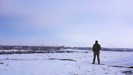 A lone person stands on a snowy hill, looking out at the distant city skyline, symbolizing a journey or a moment of quiet contemplation on a cold winter day
