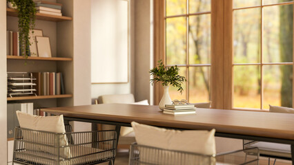 Books and vase on wooden table and metal armchairs with pillow cushion aside bookshelf and windows.