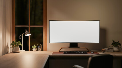 White curved screen computer with lamp on wooden table and armchair in a room corner aside window