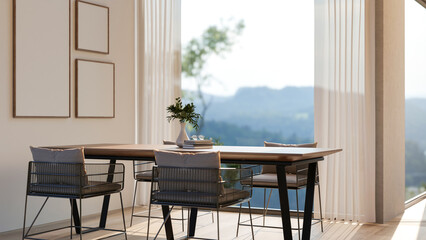 Wooden table and armchairs aside window wall with mountain scenery and blank frames on the wall.