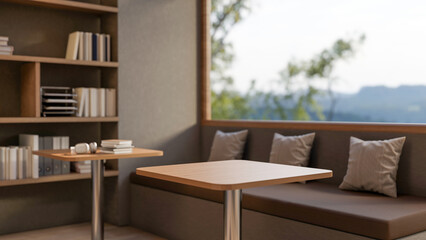 Wooden stool table and long bench with cushion pillows below glass window aside bookshelf in a cafe.