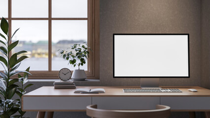 White screen computer with books and clock on wooden table aside window and plant in loft wall room.