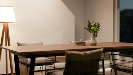 Dining wooden table with metal armchairs and high floor lamp aside white wall and staircase at night