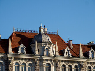 Obraz premium A detailed view of the roof of a classic, ornate European building with red tile roofs and a grand facade against a deep blue sky.