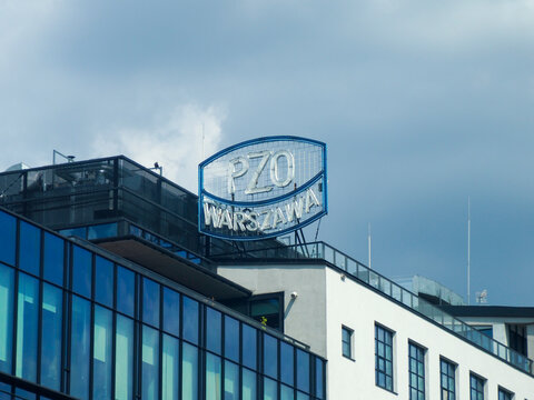 Close-up of a modern building with a PZO Warszawa sign on the rooftop against a cloudy sky.