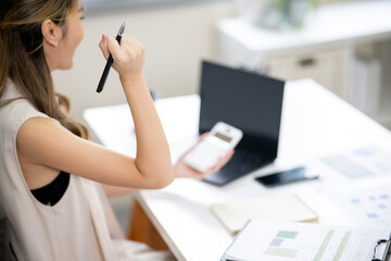 Side view of a woman office worker holding pen and calculator in front of laptop at table in office.