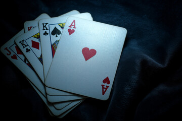 Royal flush poker cards on dark velvet background, moody lighting