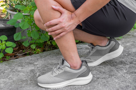Asian male athlete grips shin in pain—suggests muscle strain, shin splints, or post-exercise fatigue. Ideal for rehab, sports medicine, or recovery ads.