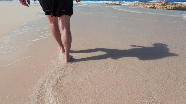 Close-up view of person walking barefoot along shoreline, with gentle waves washing over smooth sand. Tranquil coastal scene evoking summer leisure and freedom. Marsa Matrouh governorate, Egypt
