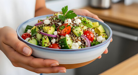 Woman holding a bowl of quinoa salad with avocado cucumber tomatoes and feta cheese