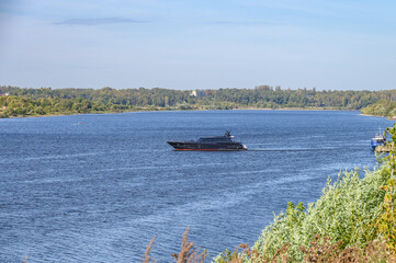 Obraz premium Luxury black yacht sails along the river against the backdrop of a forested shore.