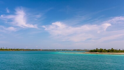 Fototapeta premium A tranquil vista of azure water meeting a tropical shoreline, highlighted by fluffy white clouds against a vibrant blue sky.