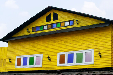 Vibrant Yellow House with Colorful Windows Against Clear Sky