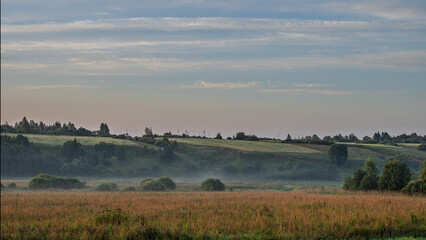 Hilly plain covered in fog, illuminated by the dawn sun.