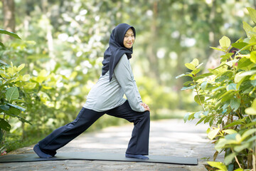 Muslim woman doing yoga in park wearing long sleeve t-shirt and black hijab