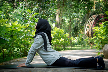 Muslim woman doing yoga in park wearing long sleeve t-shirt and black hijab
