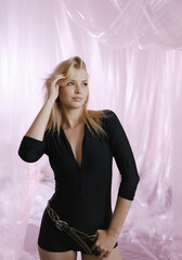 A gorgeous girl in a black tight-fitting suit with a stylish belt on a delicate airy background.