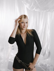 A gorgeous girl in a black tight-fitting suit with a stylish belt on a delicate airy background.
