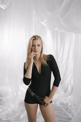 A gorgeous girl in a black tight-fitting suit with a stylish belt on a delicate airy background.