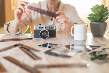 Woman holding a strip of developed film near an old vintage camera on a wooden table, reminiscing about the past and enjoying the classic manual photography process