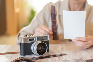 Person's hands holding an undeveloped film strip and a blank photographic print, with a vintage...