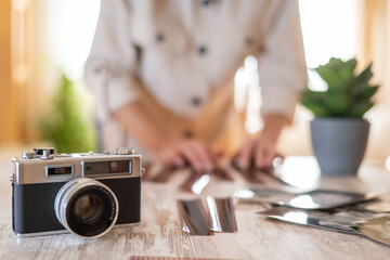 Person is arranging and viewing developed film negatives and prints on a wooden table, emphasizing...