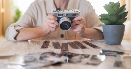 Senior woman holding a classic analog camera, revisiting memories with old negatives and prints,...