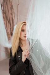 Portrait of a beautiful woman in a leather jacket near the curtain.