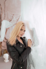 Portrait of a beautiful woman in a leather jacket near the curtain.