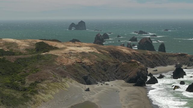 Drone flight over dunes near Crook Point at the Oregon Coast in windy conditions. Mack arch and other sea stacks in the distance.