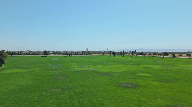 Drone ascending from soccer field into sky showing farmland and residential area.