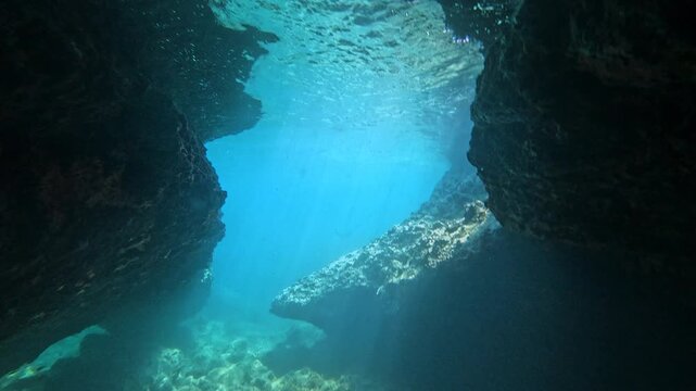 Rocky underwater cave passage with light shining into the open blue sea. Great for adventure, exploration, diving, and marine environment themes.