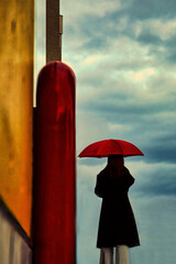 雨の予感を感じつつ曇り空を眺める赤い傘の女性