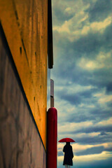 曇天を眺めながら雨を予感する赤い傘の女性