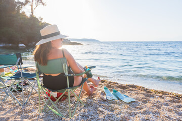 Woman relaxes on a beach chair at a pebble beach, gazing at the sea