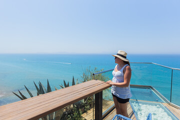Woman on balcony overlooking ocean on sunny day, coastal vacation scene