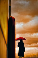 夕日を見つめる赤い傘の女性