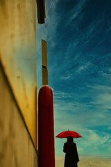 流れる雲の下で赤い傘をさす女性