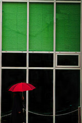 緑のアーケードを歩く赤い傘の女性