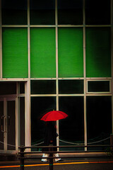 緑のアーケードを歩く赤い傘の女性