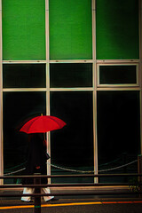 緑のアーケードを歩く赤い傘の女性