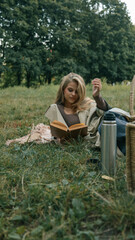 Woman enjoying a book during a relaxing picnic in a park on a sunny day.
