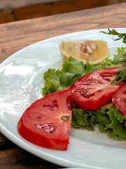 Fresh tomato slices with lettuce and lemon wedge on white plate
