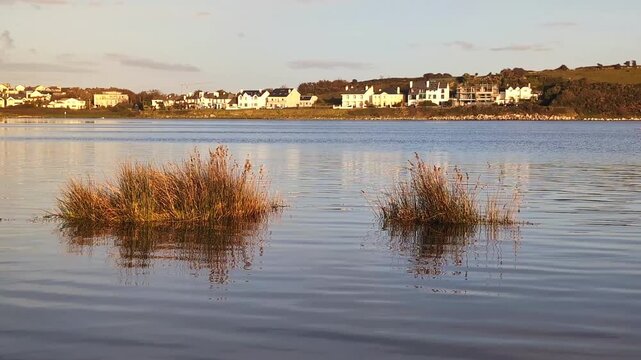 Golden Hour Sunset Over Galway Bay Near Silverstrand Beach Featuring Calm Water Reflections and Coastal Village Houses Along the Irish Shore, adventure travel backgroud