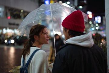 Young asian couple with umbrella on rainy night in city street