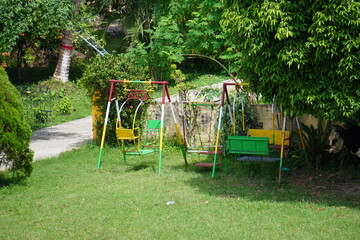 Colorful playground swings surrounded by lush green trees and grass