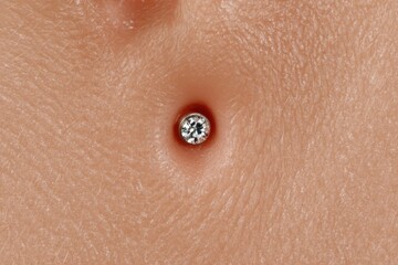 Fototapeta premium Close-up view of a stunning diamond stud placed in a well-defined piercing within smooth skin showcasing intricate textures of epidermis and highlighting personal adornment elegance